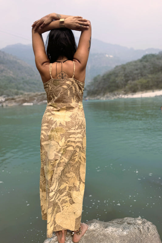 Woman in a long, patterned dress standing by a body of water with mountains in the background