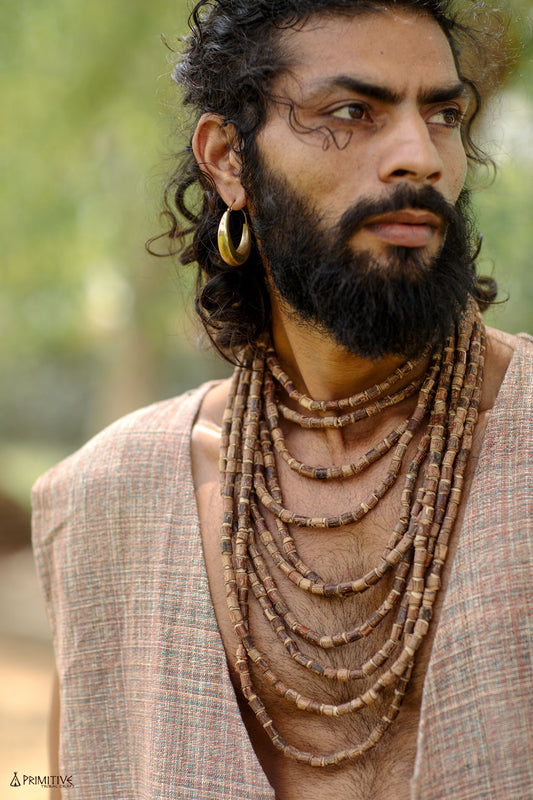 Man with long hair and beard wearing the 10-strand Tulsi wood beads necklace layered over a natural linen shirt