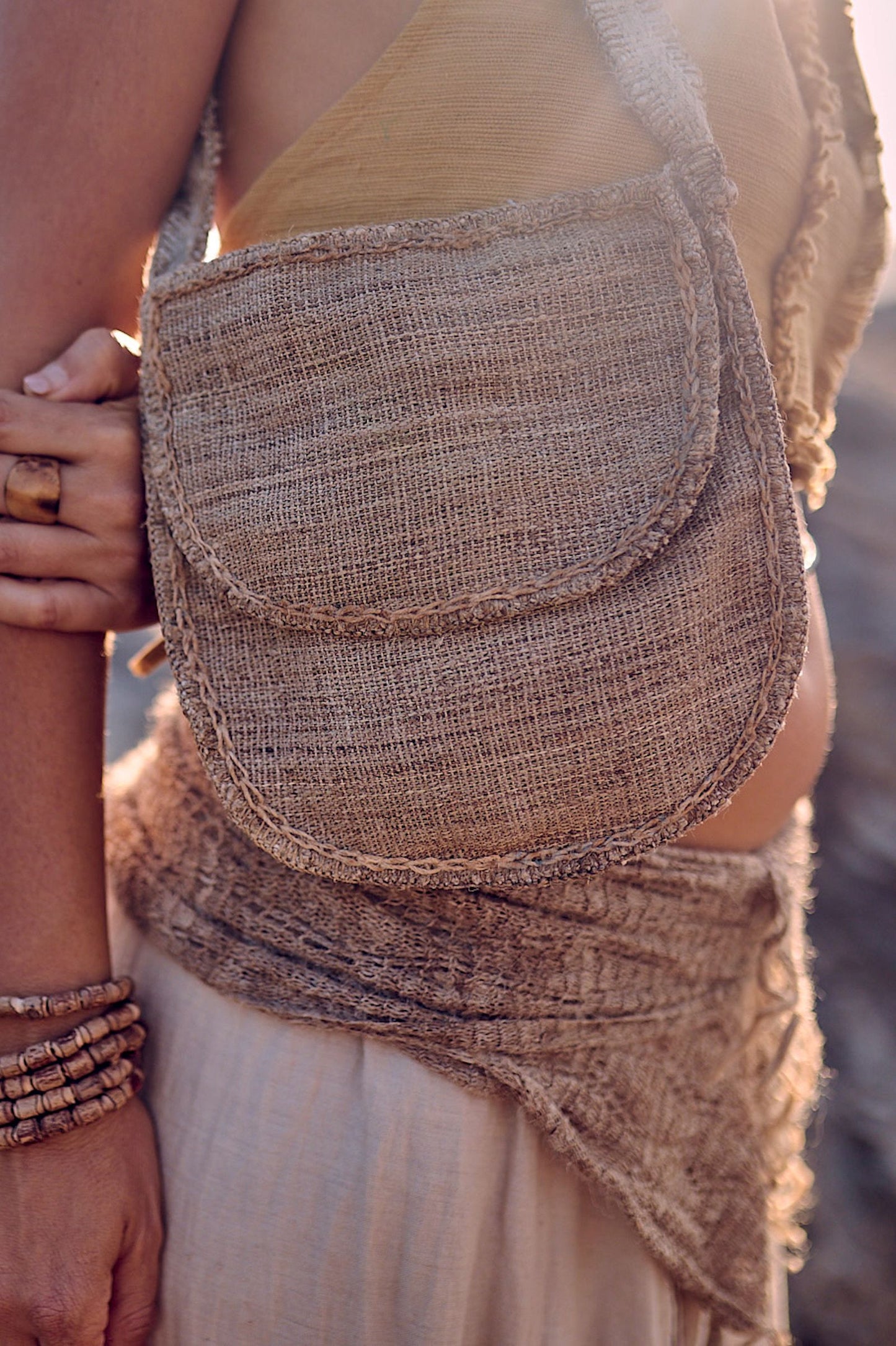Close-up of the handstitched wild nettle and hemp side bag showing the raw handwoven texture, rounded flap closure, and natural frayed edges in warm golden light