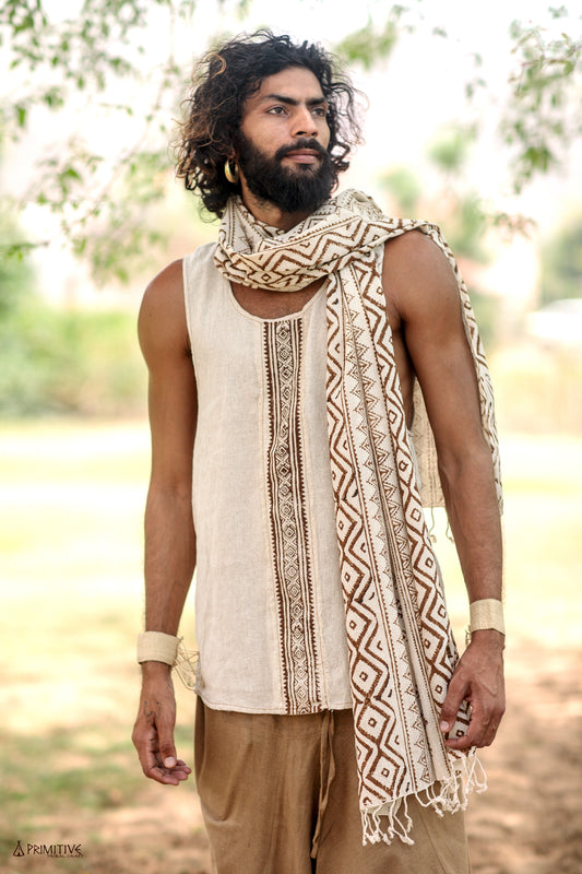 A boho man wearing a traditional beige handwoven raw silk tank top with brown block print patterns, paired with a white scarf, standing outdoors.