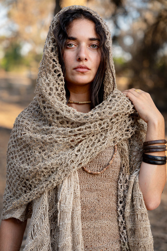Close-up portrait of a woman wearing a 100% Wild Himalayan Nettle hooded shawl, showing the intricate open-knit texture and natural beige fiber.