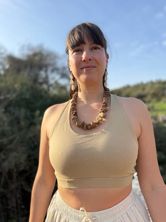 Woman wearing a soft stretchy lycra yoga top in a sand tone, front view in natural outdoor light.