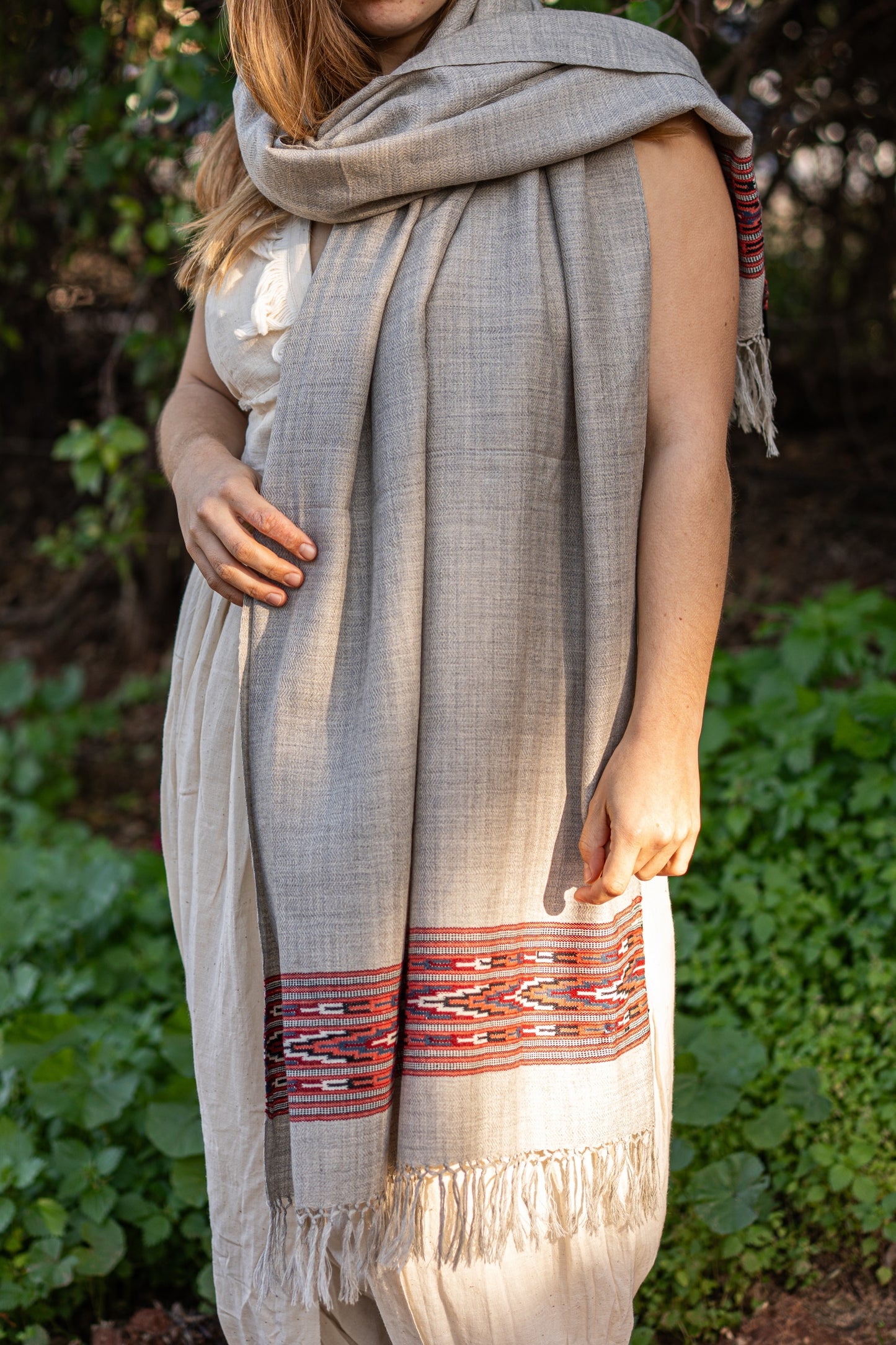 Light grey handwoven wool shawl featuring a traditional red and black geometric Kullu border. Authentic Indian tribal fashion for winter warmth