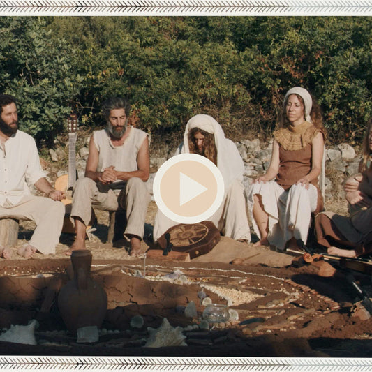 Community gathering in nature with a drum in the center, participants wearing organic, earth-tone clothing and raw silk shirts and dresses