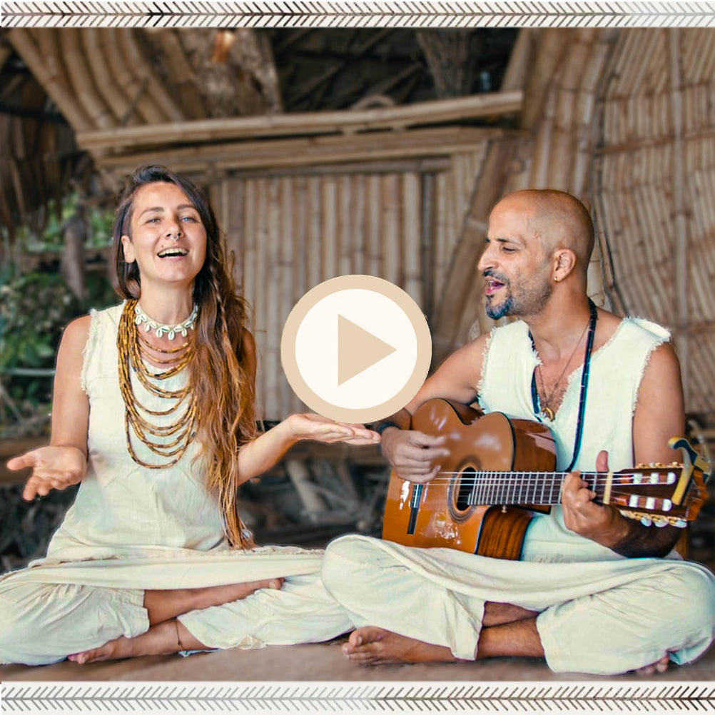 Two musicians performing a devotional song indoors, woman singing and man playing guitar, dressed in organic earth-tone outfits.