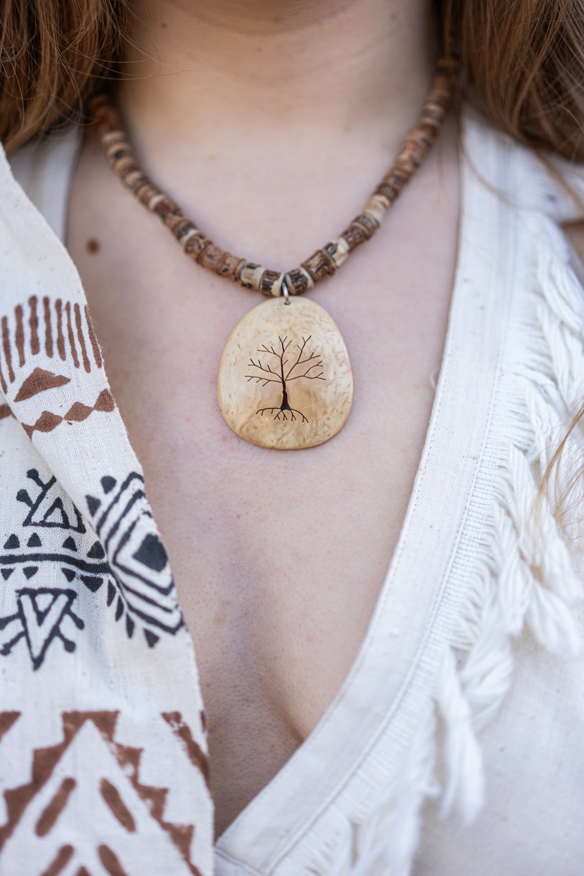 Necklace with a tree pendant worn by a person in a white garment with tribal patterns.