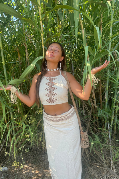 Full-body view of a Boho Woman in a raw silk halter top with tribal block print, standing among tall green reeds in natural sunlight.