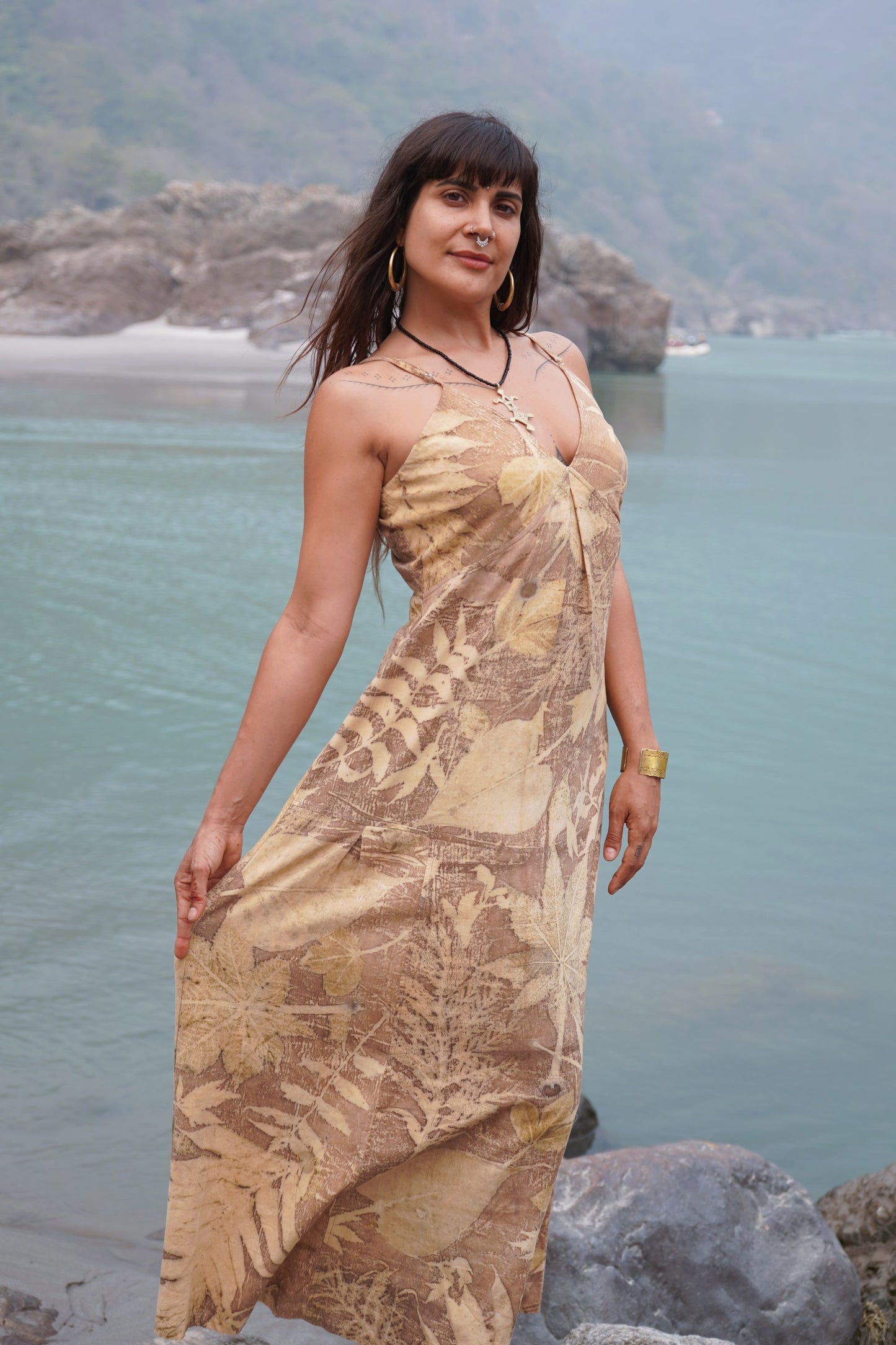Woman wearing a botanical dye long slip dress with natural leaf prints, standing by a river.