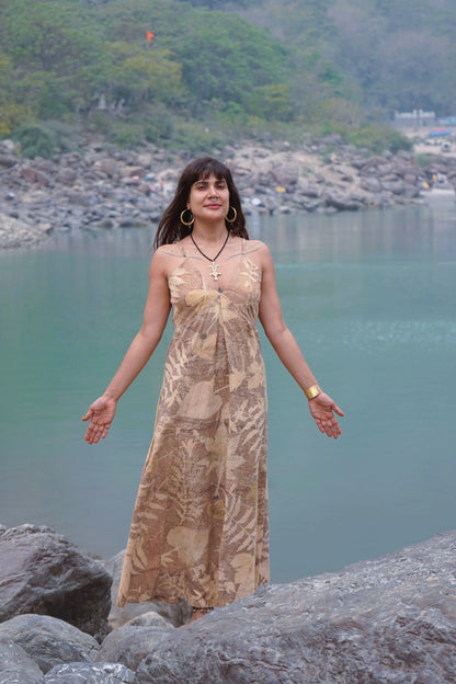 Woman modeling a botanical print maxi dress in size medium, featuring earthy brown tones and natural plant dyes, standing in a natural landscape.