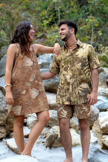Smiling couple outdoors wearing matching earthy brown botanical print clothing: a shirt set and a slip dress.