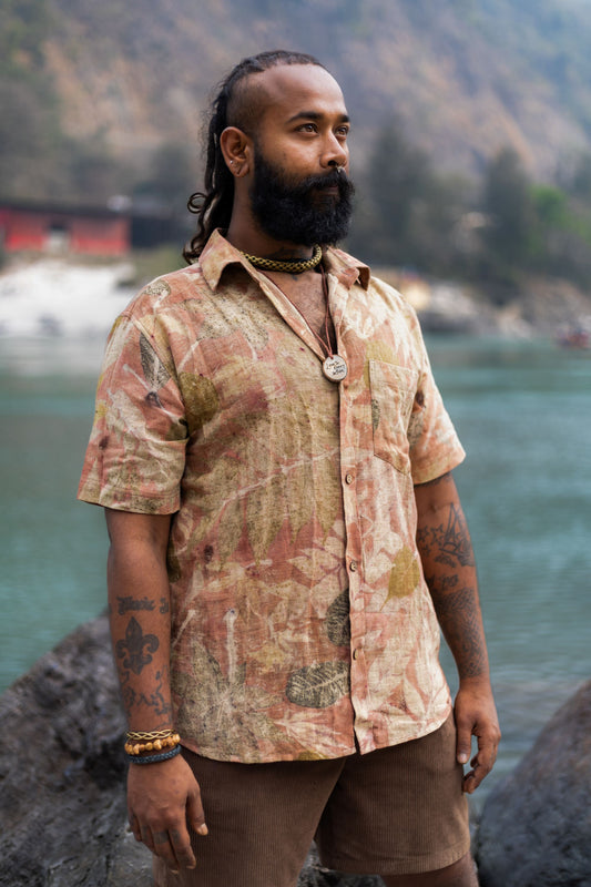Man standing by a river wearing a short sleeve botanical print buttoned shirt. Earthy pinkish brown eco dyed menswear