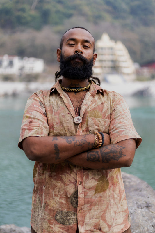 Portrait of a man with crossed arms wearing a brown eco print short sleeve buttoned shirt. Sustainable tribal style menswear.