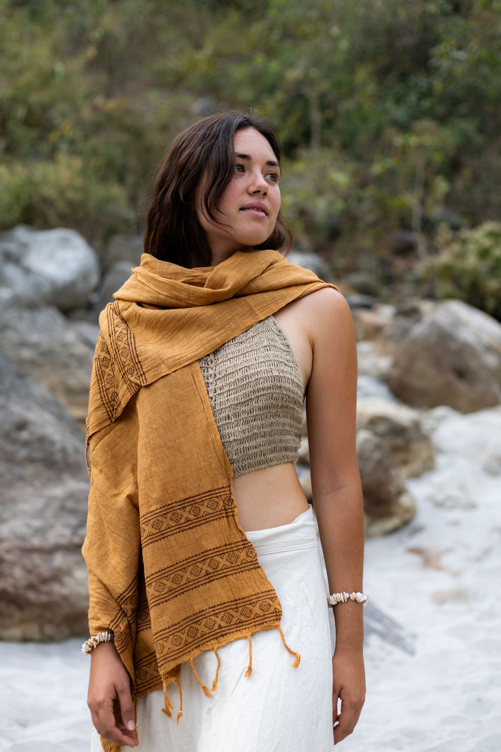 Woman looking over her shoulder wearing a handmade brown cotton wrap. Earthy boho style scarf featuring tribal block print borders and fringes.