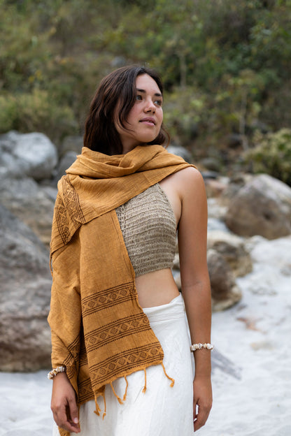 Woman looking over her shoulder wearing a handmade brown cotton wrap. Earthy boho style scarf featuring tribal block print borders and fringes.