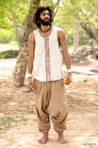 An Earthy man wearing a beige hand block print silk tank top and brown harem pants, standing outdoors.