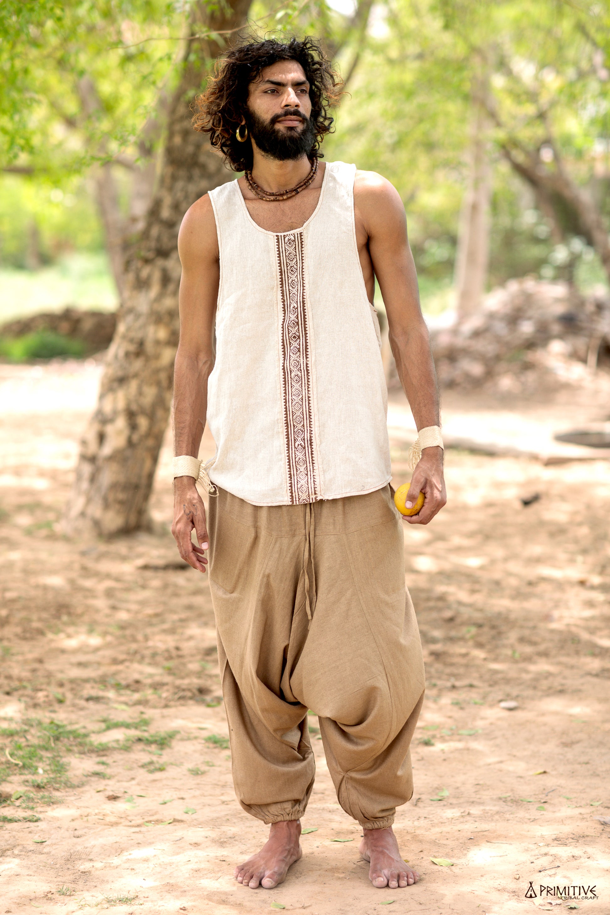 An Earthy man wearing a beige hand block print silk tank top and brown harem pants, standing outdoors.
