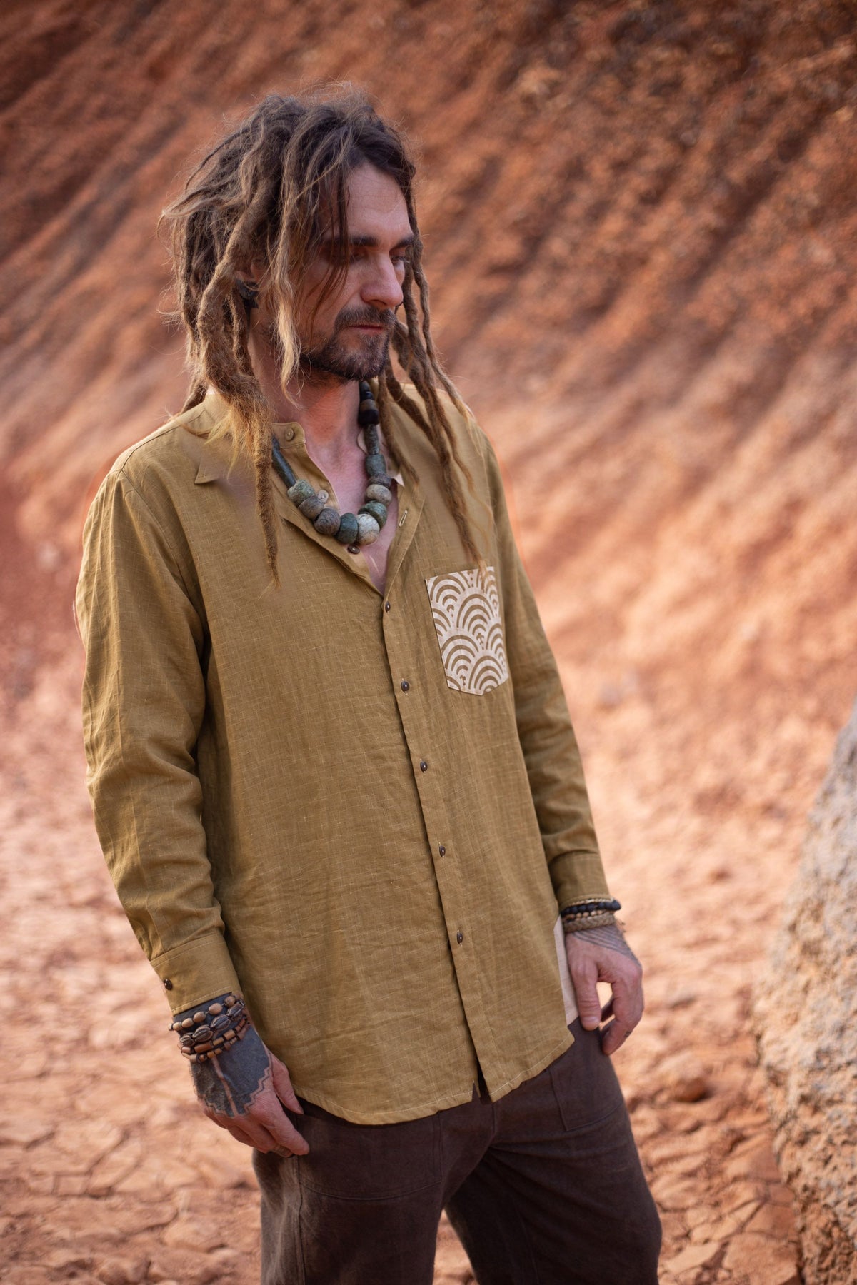 Men wearing an olive-brown handwoven linen shirt with long cuffed sleeves and a cream chest pocket with a brown wave pattern.