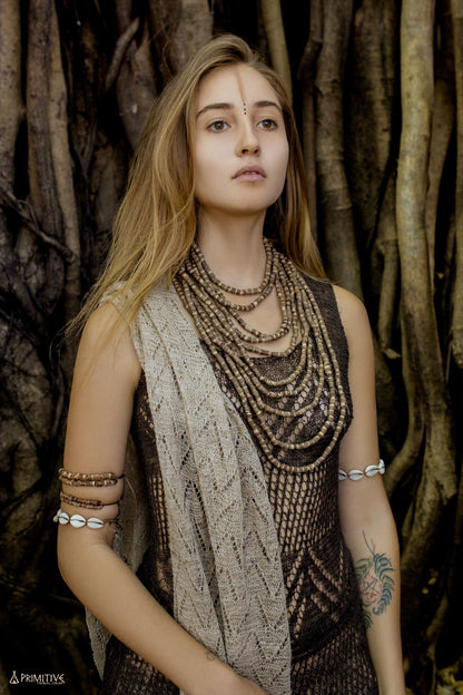 Woman wearing a large multi-strand Tulsi wood beads necklace draped in cascading layers over a natural woven top,
 posed in front of a banyan tree