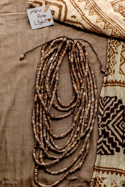 Flat lay of the 10-strand Tulsi wood beads necklace arranged on a patterned tribal textile, showing the full spread of hand-cut unpolished beads and natural brown wood tones