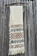 Natural khadi cotton scarf with brown tribal pattern bands and fringe, photographed hanging on a bamboo fence.