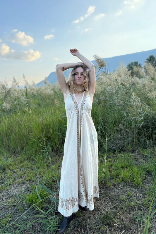 Natural cotton long butterfly dress with V-neck and block printed trim, worn by a model in a grassy field.