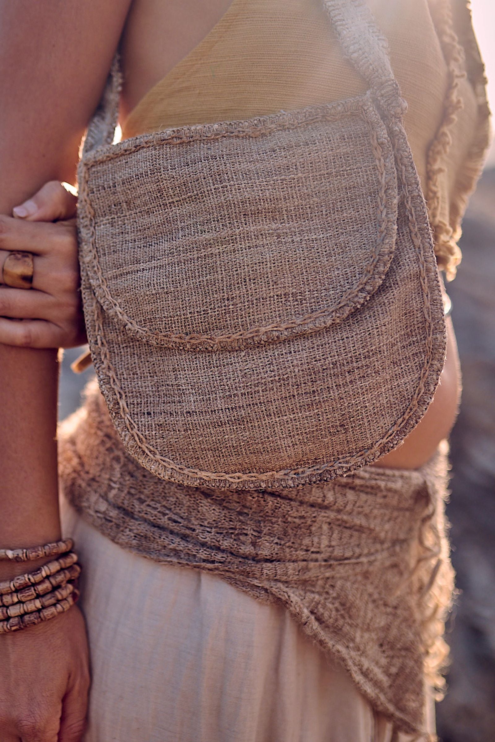 Close-up of the handstitched wild nettle and hemp side bag showing the raw handwoven texture, rounded flap closure, and natural frayed edges in warm golden light