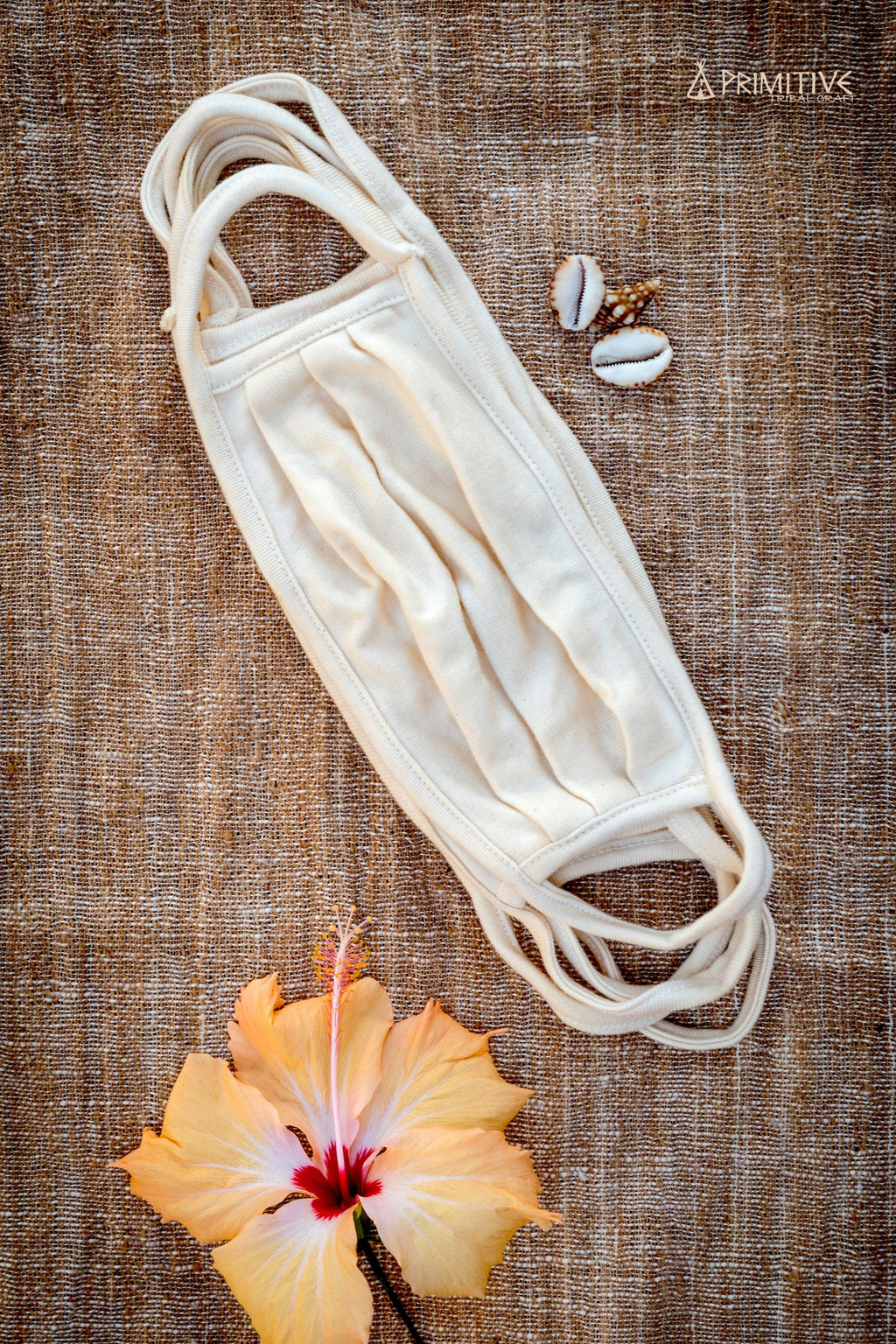 White Organic Cotton face mask on a textured brown background with a flower and shells