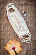 White Organic Cotton face mask on a textured brown background with a flower and shells