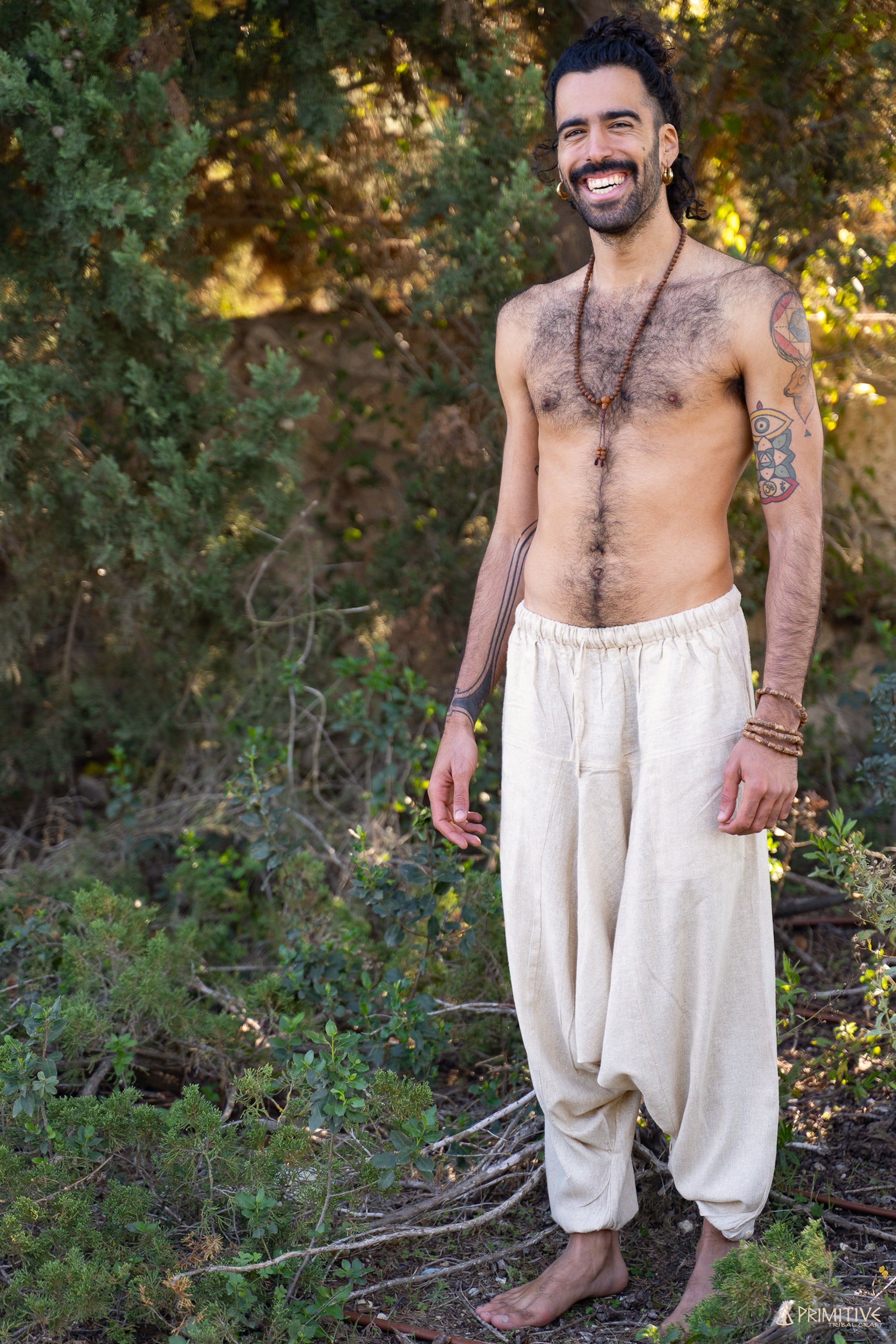 A person standing in a natural outdoor setting, wearing handwoven raw silk afghani pants in a natural color.