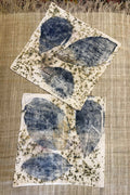 Two flat botanical print pillowcases with blue leaf vein prints, soft pink tones and olive speckles on cream cotton, laid on natural handwoven fabric