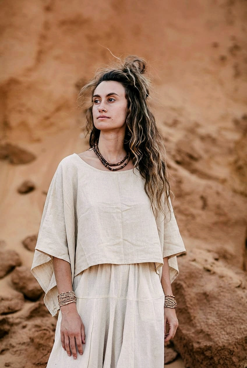 A woman standing against a sandy desert backdrop, wearing an earthy, oversized crop top made of handwoven natural beige raw silk.