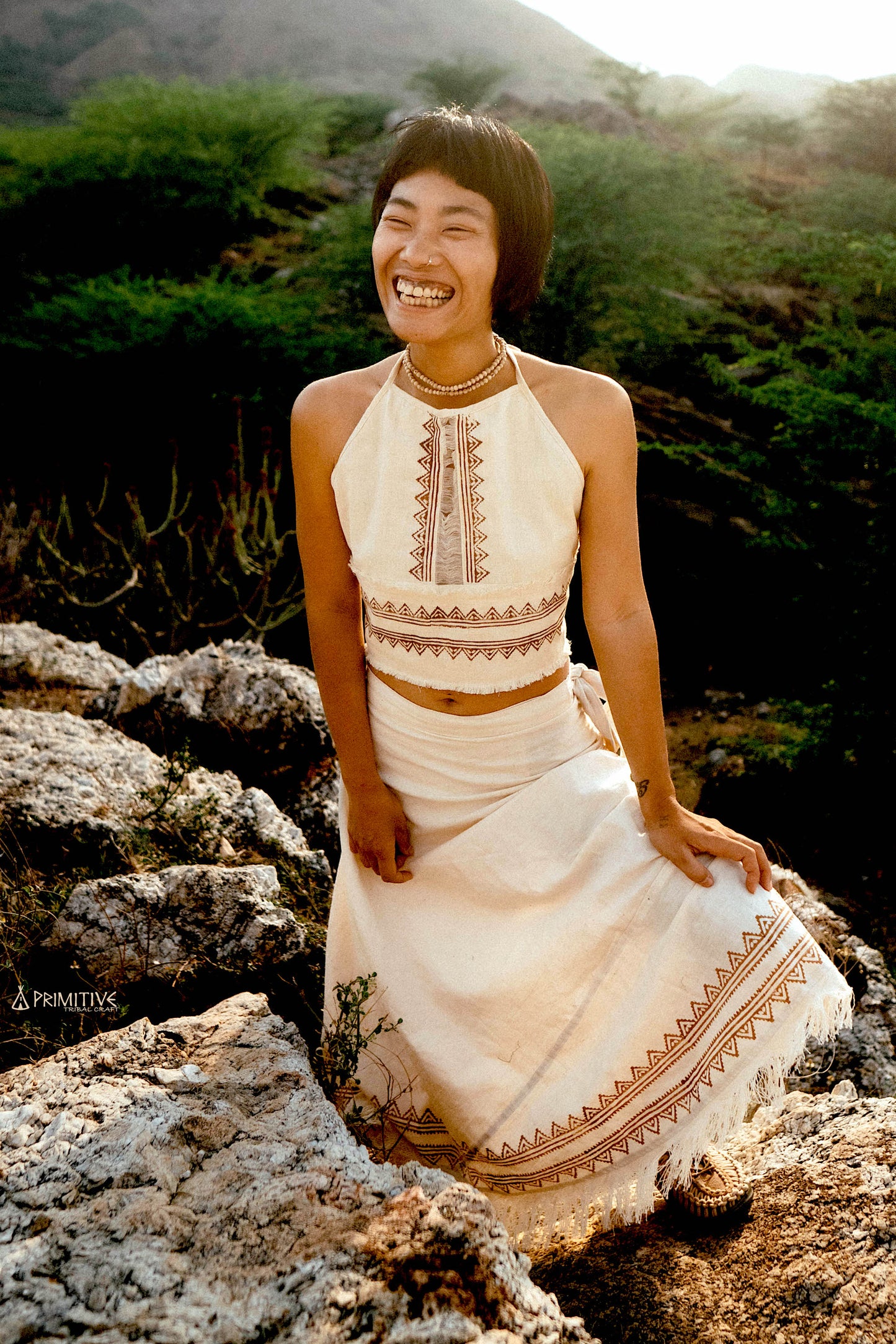 A woman wearing a lightweight white handwoven cotton top with subtle tribal block prints, standing in soft natural light