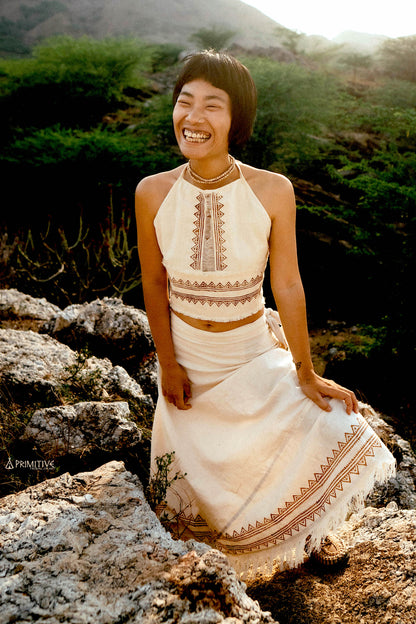 A woman wearing a lightweight white handwoven cotton top with subtle tribal block prints, standing in soft natural light