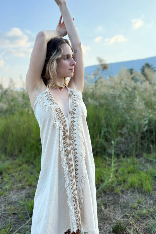 Model wearing a short butterfly cotton dress with a deep V-neck, fringed edges, and brown geometric trim, photographed outdoors.