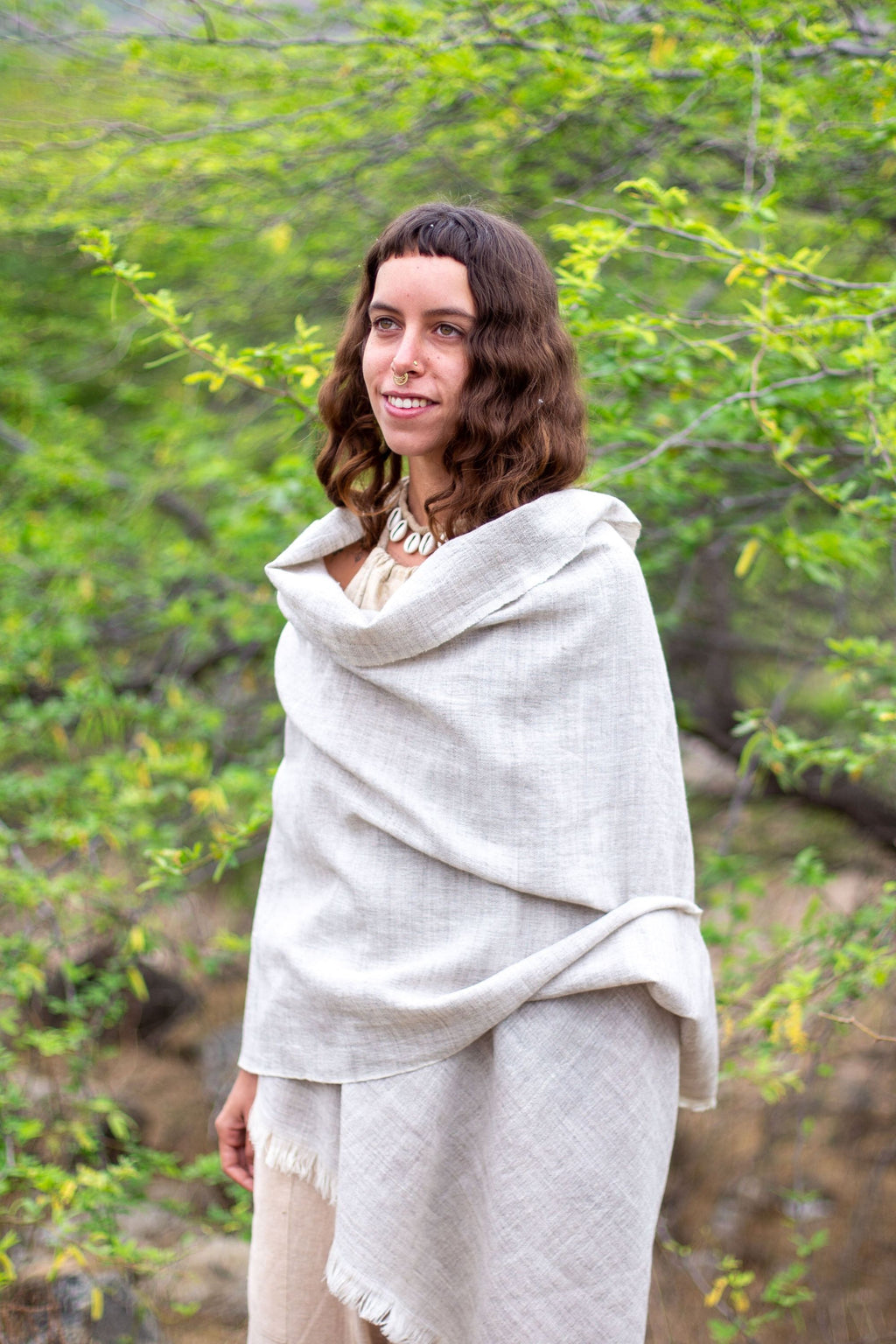 Woman wrapped in a handwoven Grey Wool Shawl standing in a natural setting with greenery.