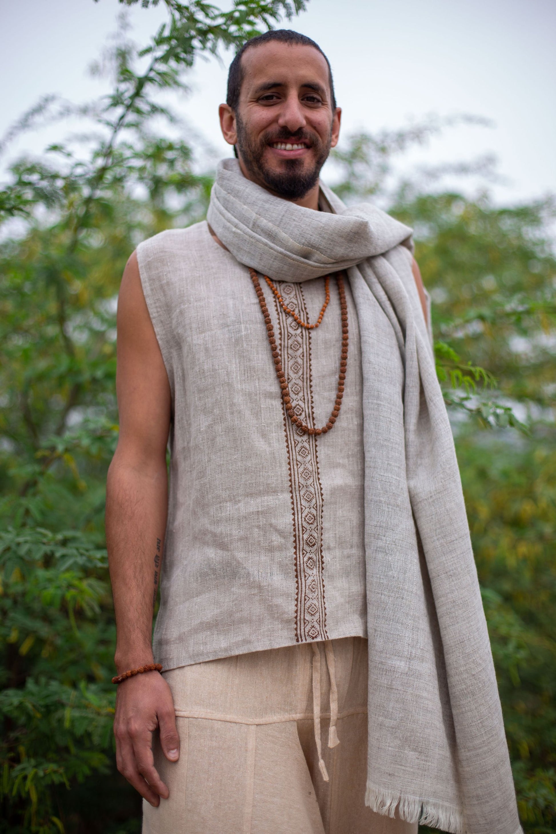 Man wearing Thin Handwoven Grey Wool Shawl necklace, standing outdoors with greenery in the background