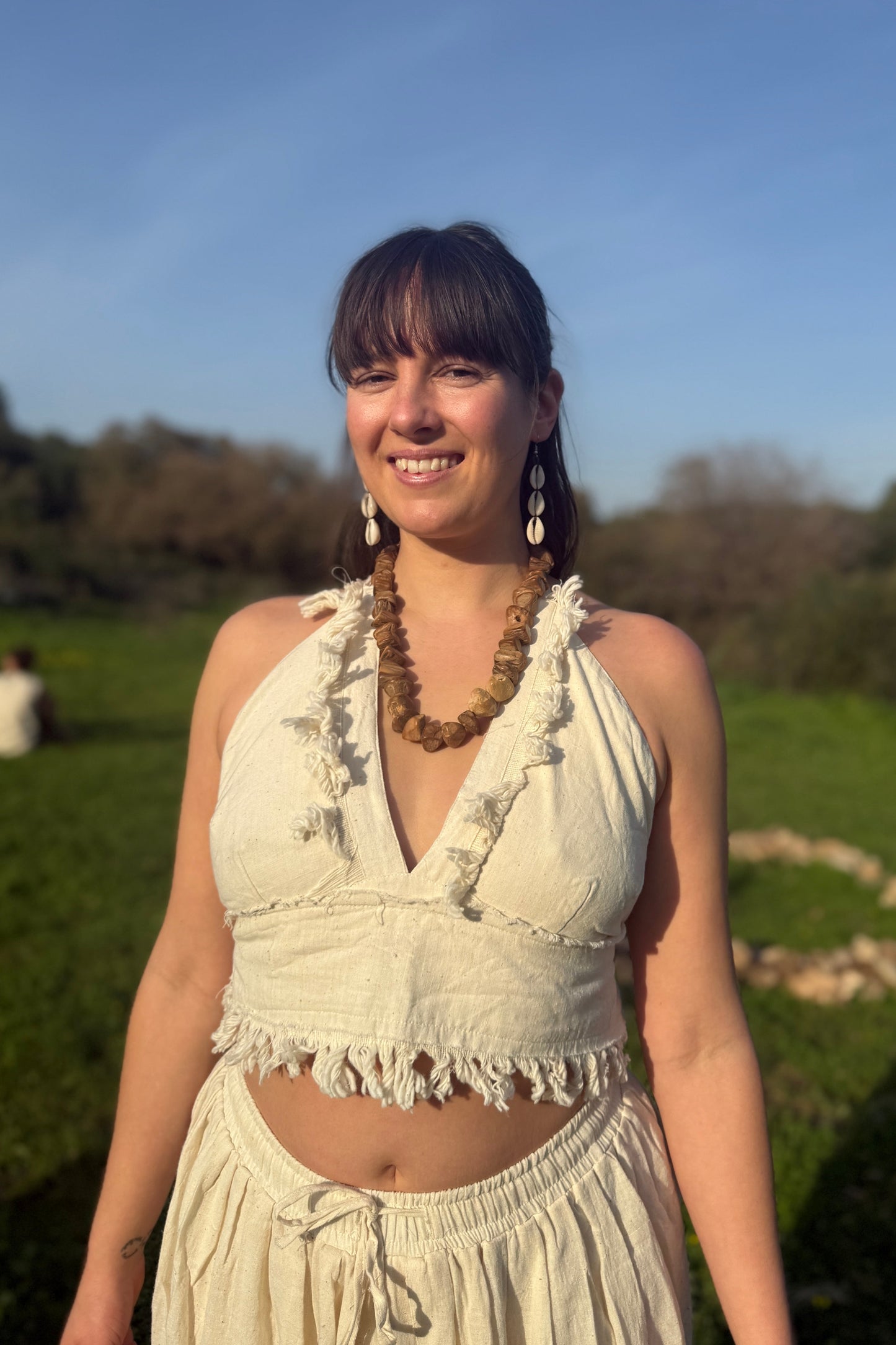 Close-up of a woman wearing a natural khadi cotton halter top with V-neck and frayed fringe trim, outdoors in sunlight