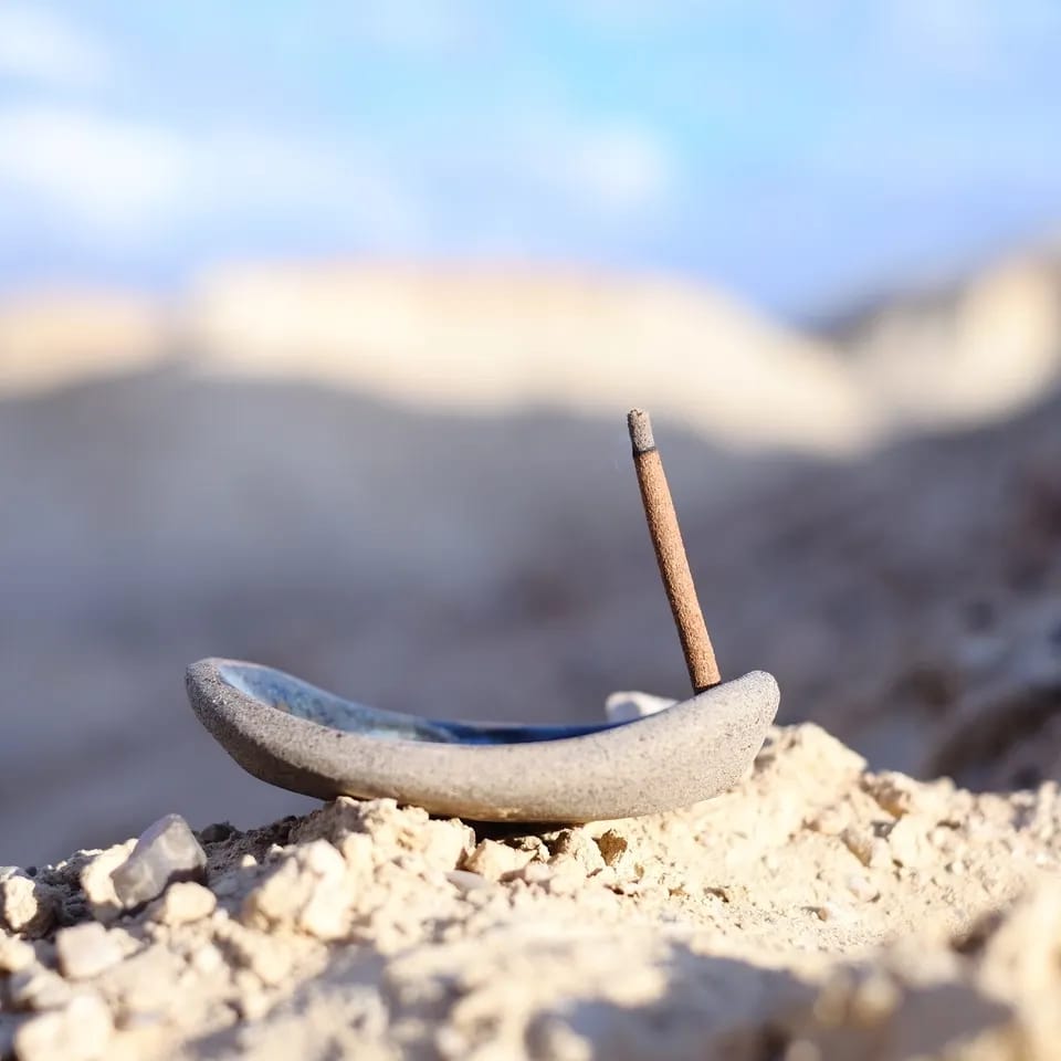 Ceramic incense holder with an incense stick on a rocky surface with a blurred natural background