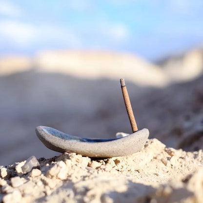 Ceramic incense holder with an incense stick on a rocky surface with a blurred natural background
