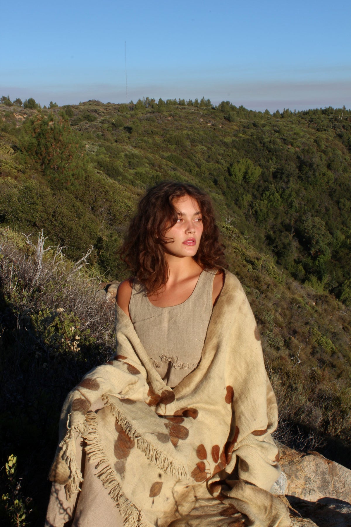 Woman seated in nature wearing the handspun and handwoven Ancient Path wool shawl with natural botanical eco prints.