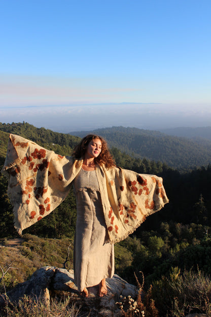 Woman wearing the Ancient Path handwoven pure wool shawl with botanical eco print, standing on a mountain overlooking a forest landscape.