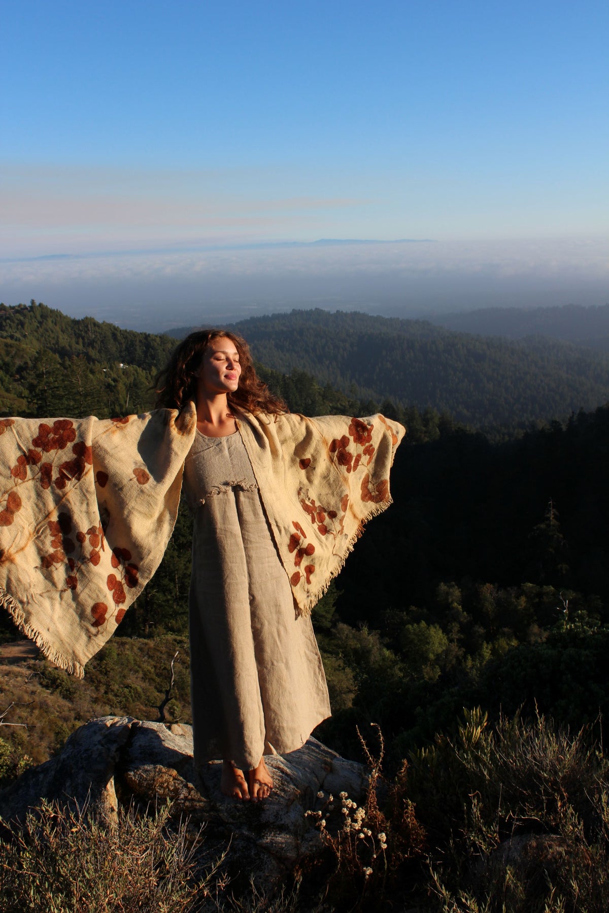 Woman displaying the Ancient Path pure wool shawl with botanical leaf prints, handwoven from natural local wool in a mountain landscape.