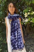 Woman wearing a blue tie-dye scarf outdoors with greenery in the background