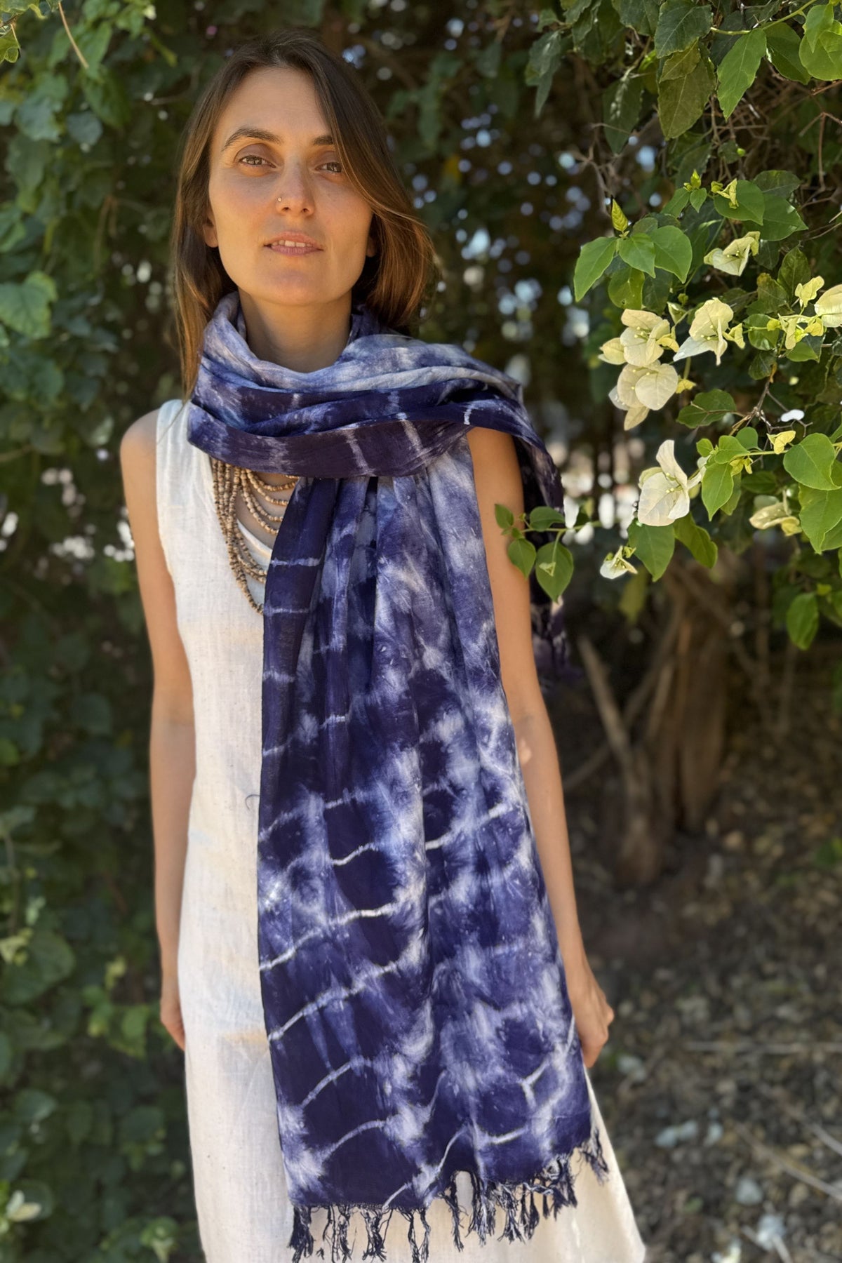 Woman wearing a blue tie-dye scarf outdoors with greenery in the background