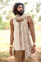 A boho man wearing a traditional beige handwoven raw silk tank top with brown block print patterns, paired with a white scarf, standing outdoors.