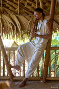 Model wearing natural cotton harem pants with relaxed drop-crotch fit and drawstring waist, styled for boho yoga and laid-back lifestyle in a bamboo hut