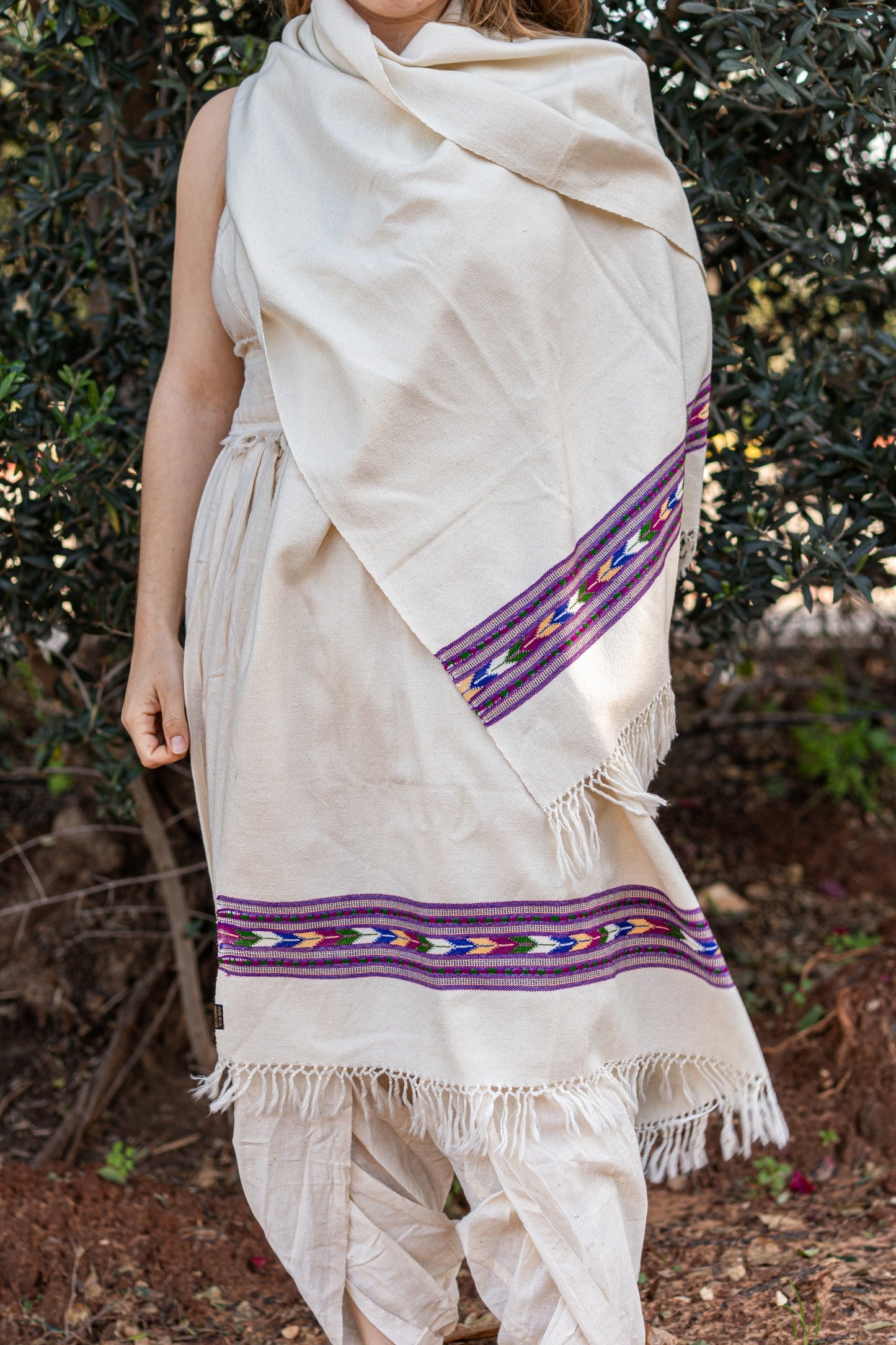 Woman wearing a creamy white traditional Kullu shawl made of pure wool. The shawl features a vibrant purple  geometric tribal border, styled as a bohemian wrap