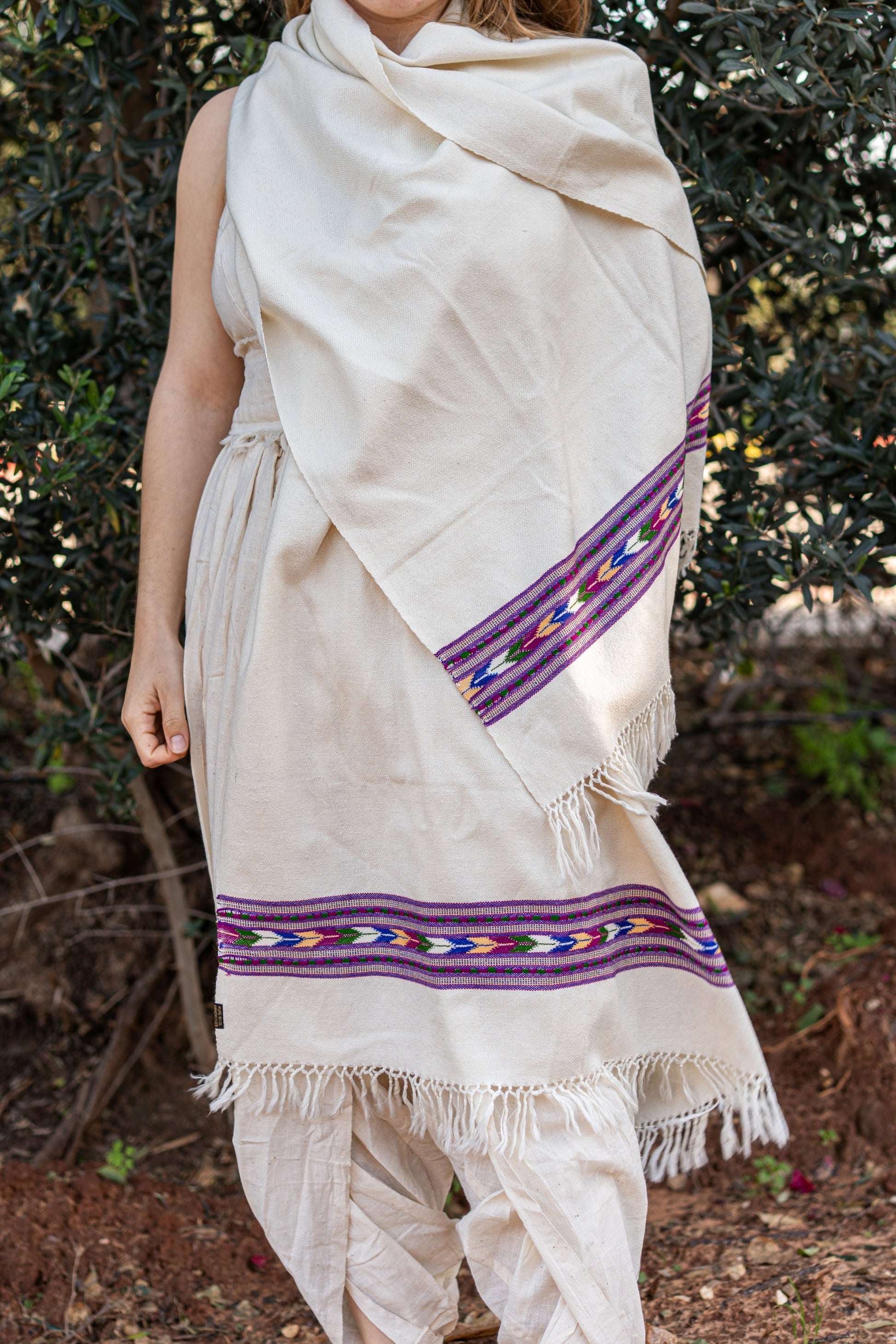 Woman wearing a creamy white traditional Kullu shawl made of pure wool. The shawl features a vibrant purple  geometric tribal border, styled as a bohemian wrap