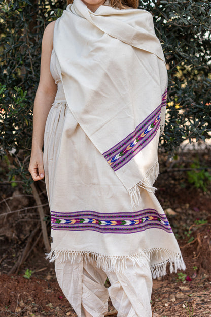 Woman wearing a creamy white traditional Kullu shawl made of pure wool. The shawl features a vibrant purple  geometric tribal border, styled as a bohemian wrap