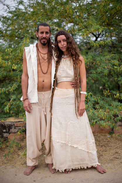 Two people in natural, earthy clothing standing outdoors with greenery in the background.